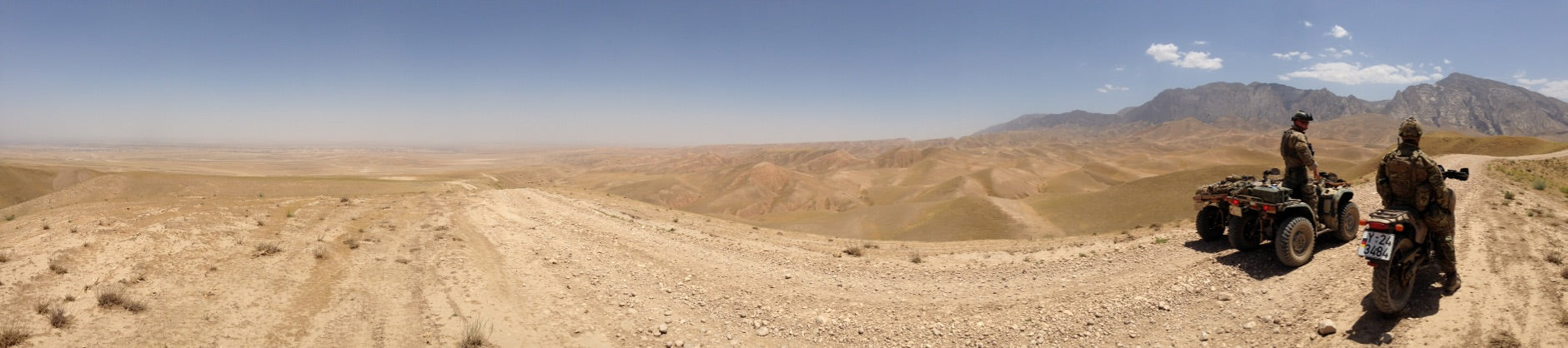 Two operators riding ATVs in a remote desert mountain landscape during a tactical mobility exercise