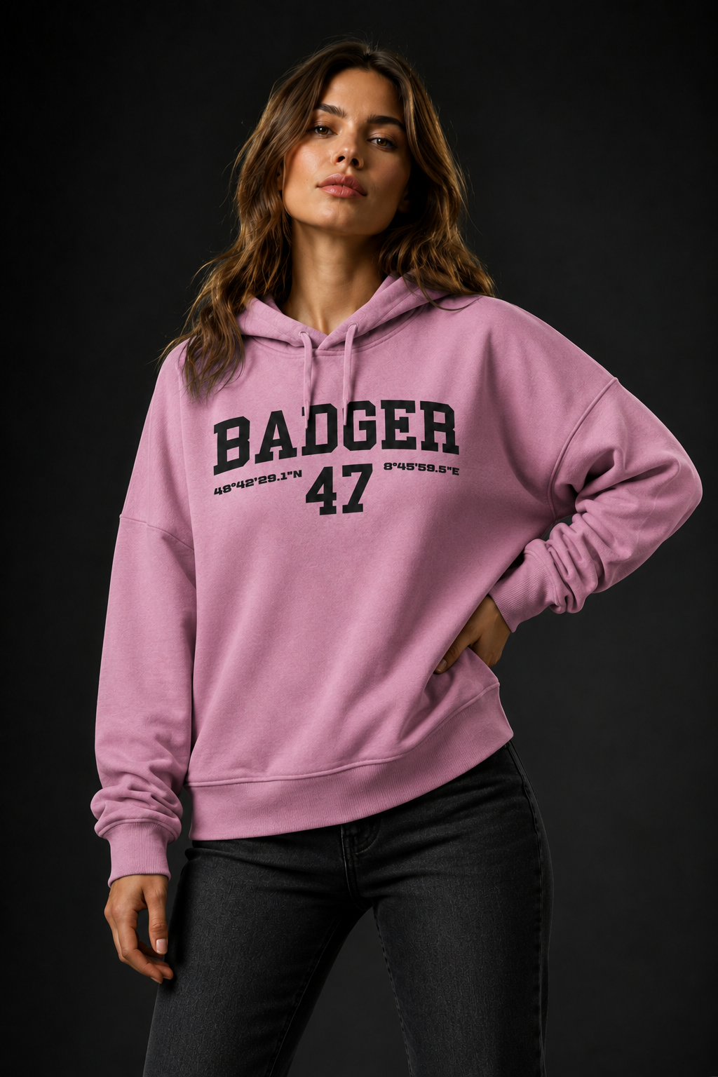 Frauenmodel trägt den BADGER 47 Hoodie in Bubble Pink vor dunklem Studiohintergrund
