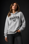 Frauenmodel trägt den BADGER 47 Hoodie in Cool Heather Grey vor dunklem Studiohintergrund
