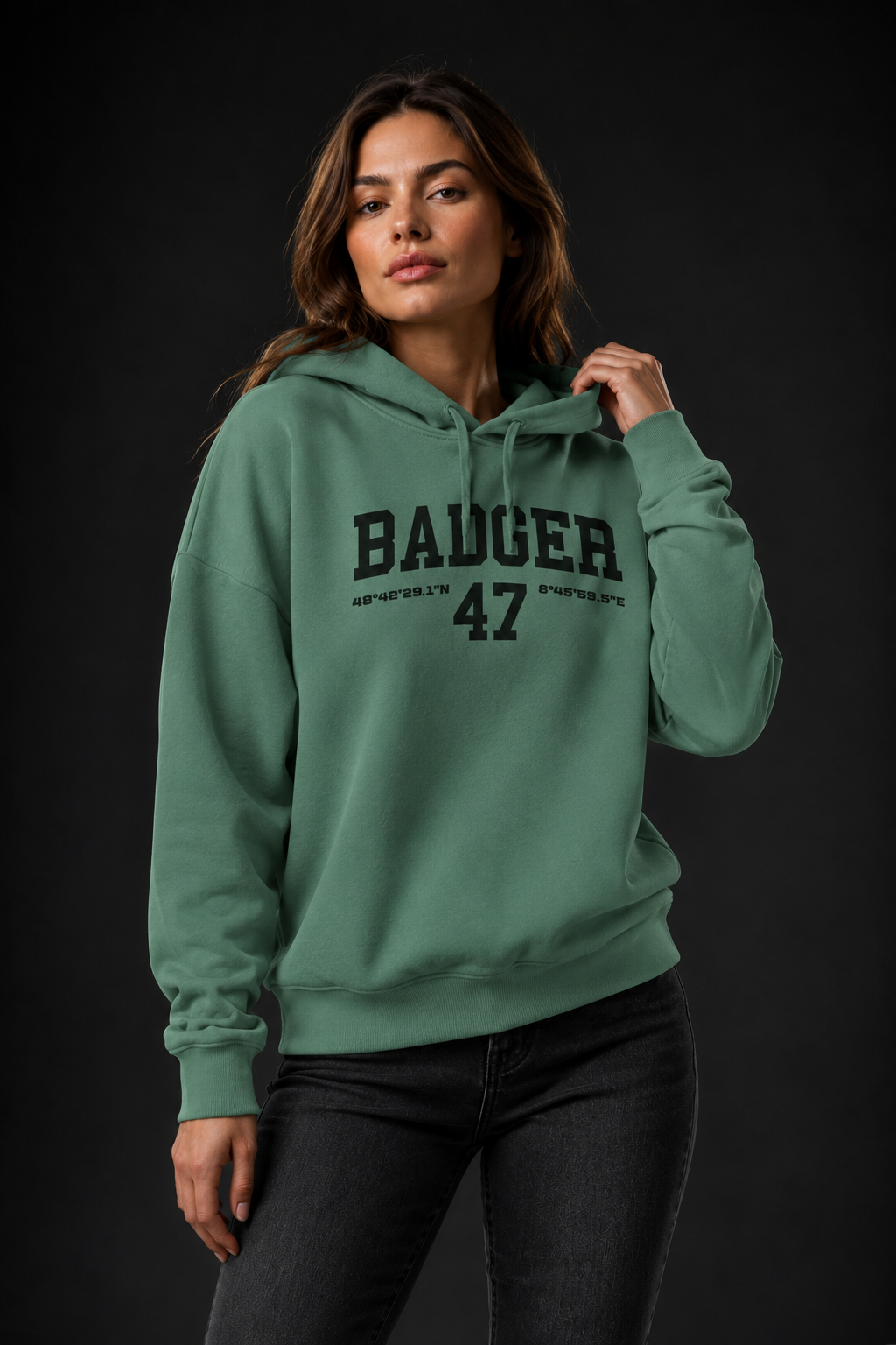 Frauenmodel trägt den BADGER 47 Hoodie in Green Bay mit einer Hand an der Kapuze
