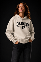 Frauenmodel trägt den Natural Raw BADGER 47 Hoodie mit beiden Händen in den Hosentaschen
