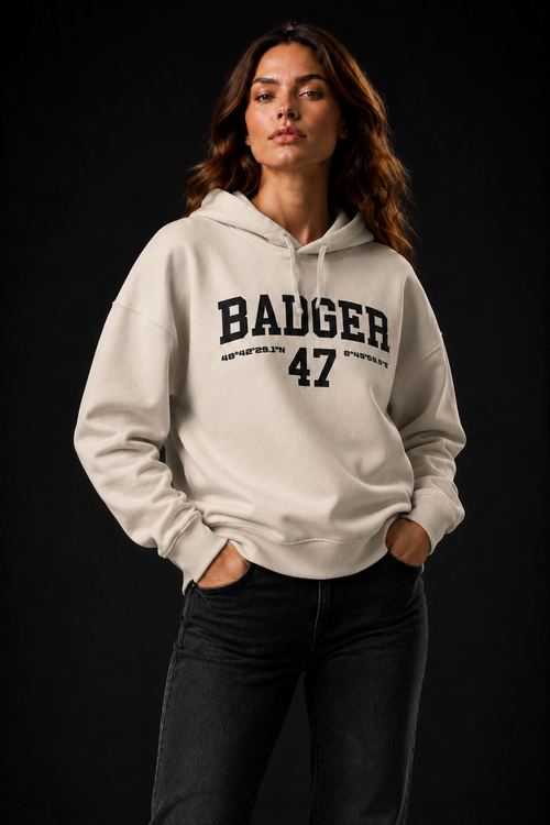 Frauenmodel trägt den Natural Raw BADGER 47 Hoodie mit beiden Händen in den Hosentaschen