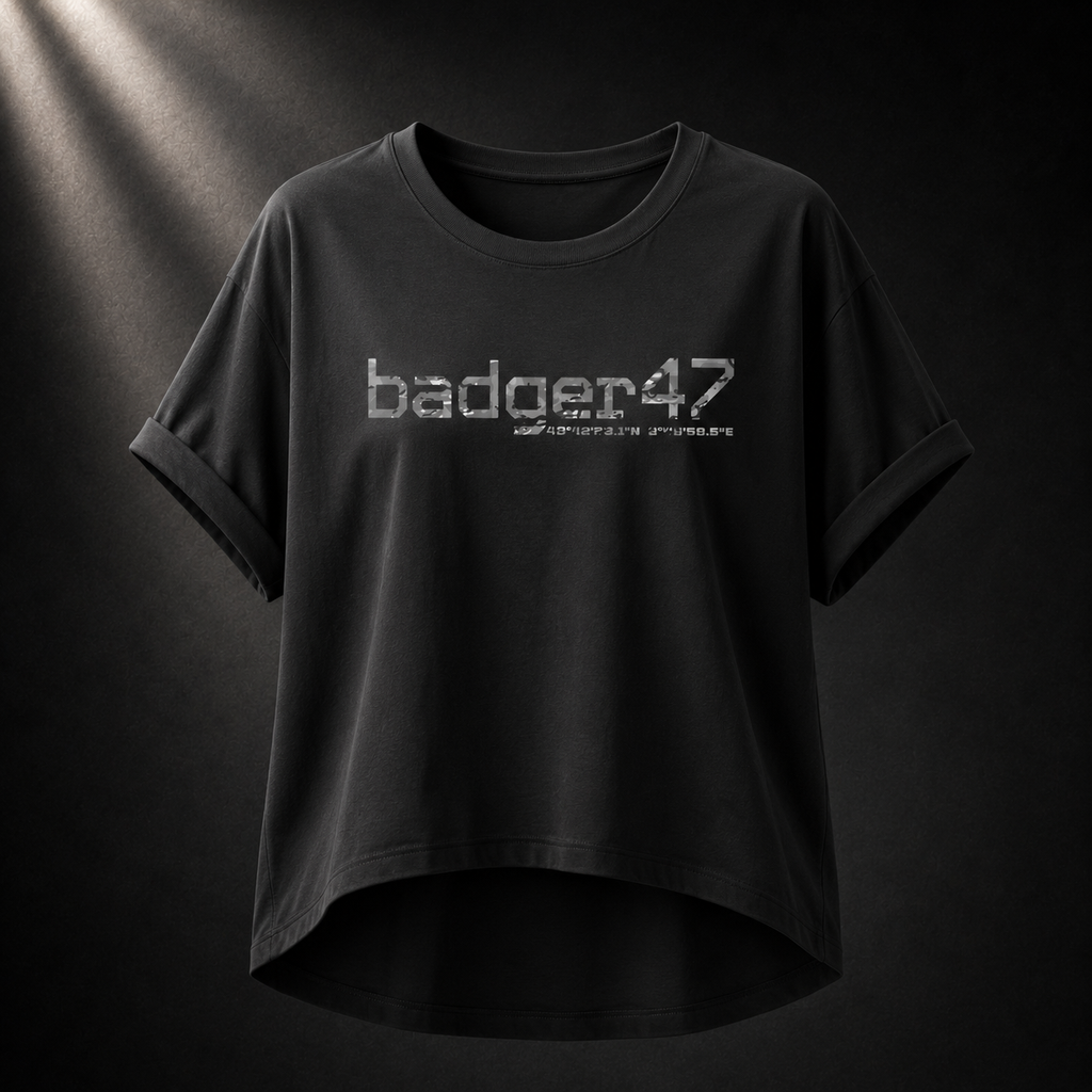 Schwarzes Badger 47 Multicam Grau Damen-T-Shirt mit weitem Schnitt, gerollten Ärmeln, längerem Rückensaum und grauem Camouflage-Logo vor dunklem Studiohintergrund
