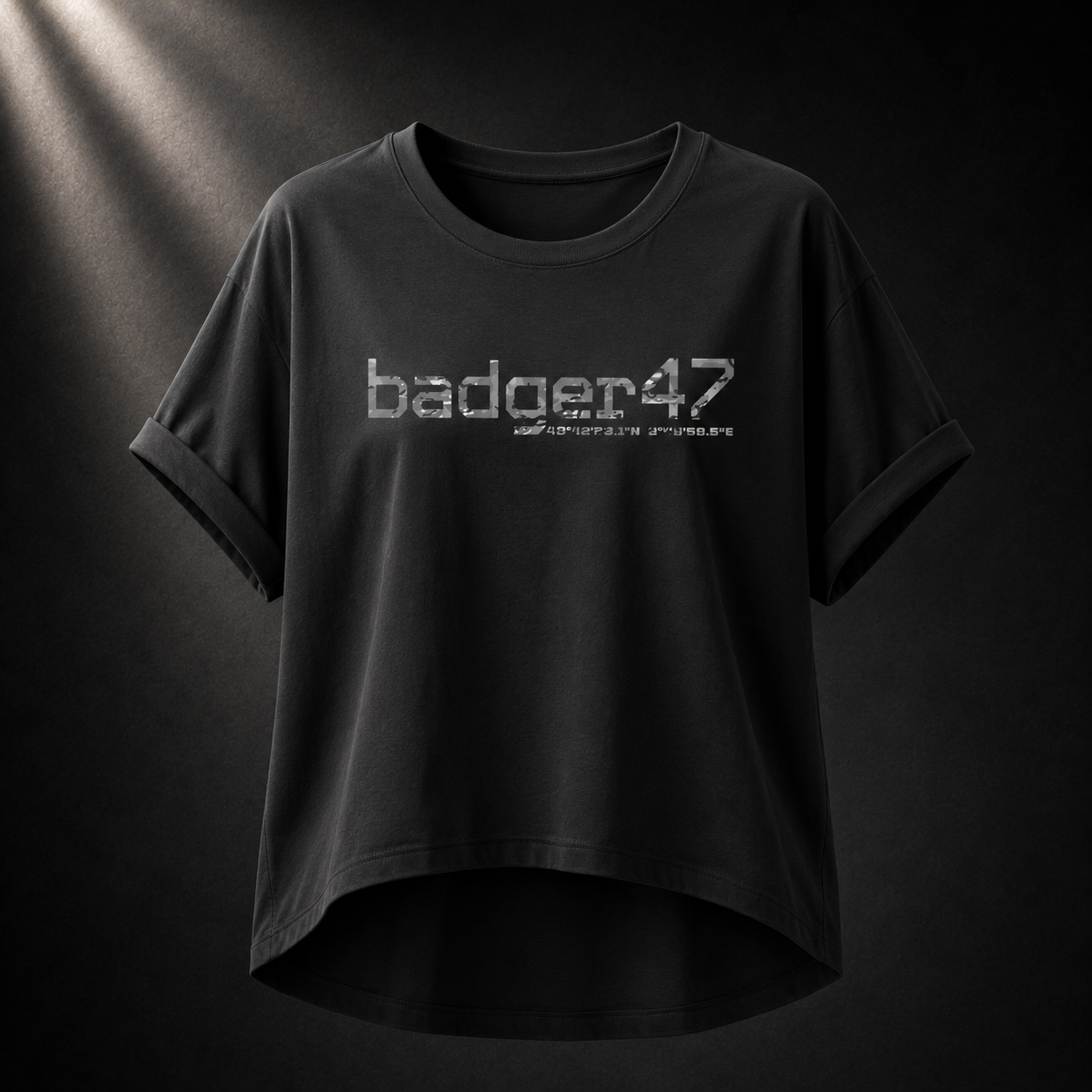 Schwarzes Badger 47 Multicam Grau Damen-T-Shirt mit weitem Schnitt, gerollten Ärmeln, längerem Rückensaum und grauem Camouflage-Logo vor dunklem Studiohintergrund
