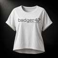 Weißes Badger 47 Multicam Grau Damen-T-Shirt mit weitem Schnitt, gerollten Ärmeln, längerem Rückensaum und grauem Camouflage-Logo im Studiolicht

