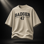 Beigefarbenes Badger 47 Varsity Oversized T-Shirt in Stone mit schwarzem College-Print im dramatischen Studiolicht

