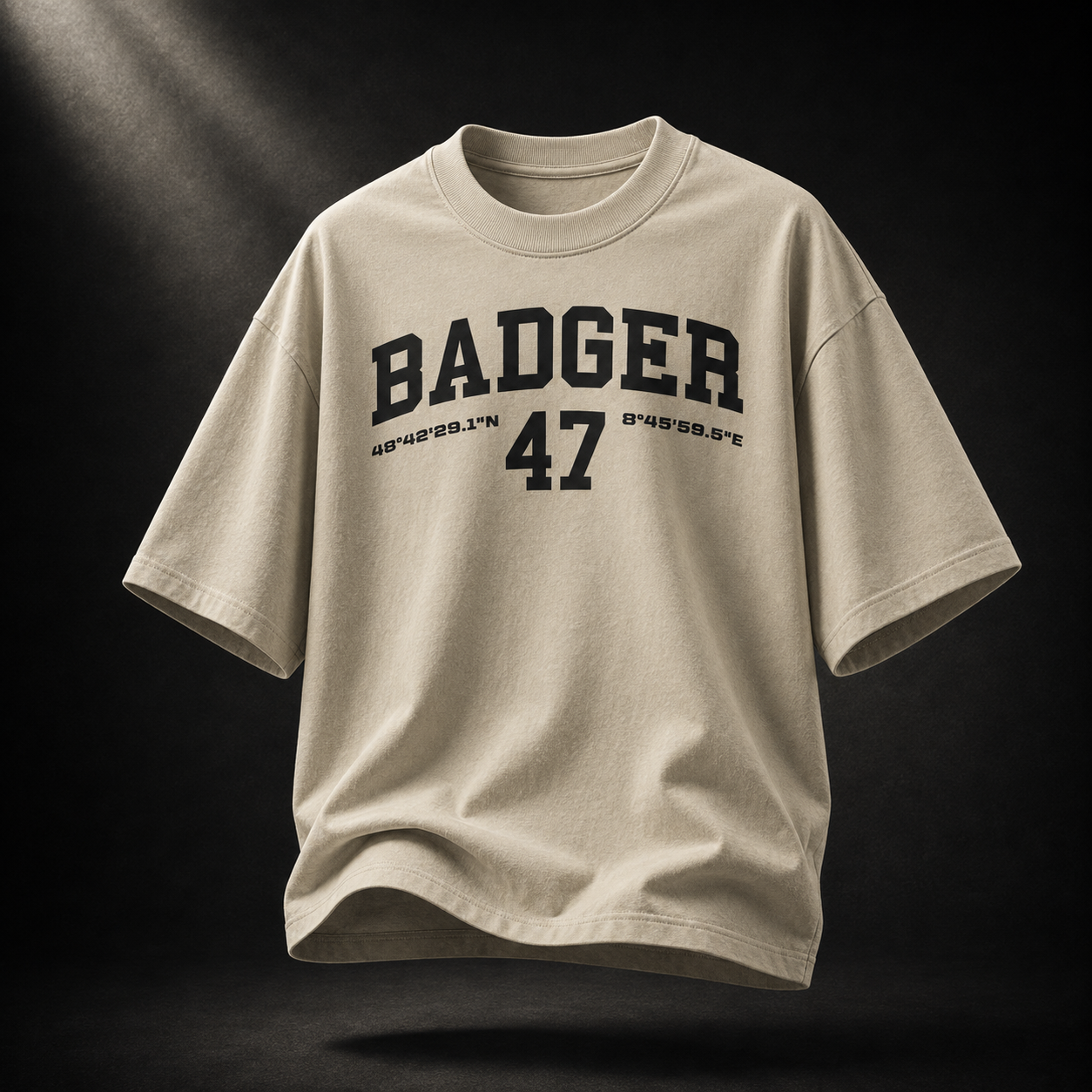 Beigefarbenes Badger 47 Varsity Oversized T-Shirt in Stone mit schwarzem College-Print im dramatischen Studiolicht
