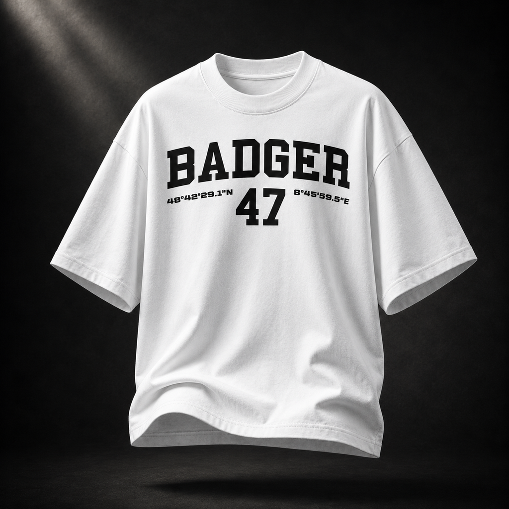 Weißes Badger 47 Varsity Oversized T-Shirt mit schwarzem College-Print, schwebend vor dunklem Studiohintergrund
