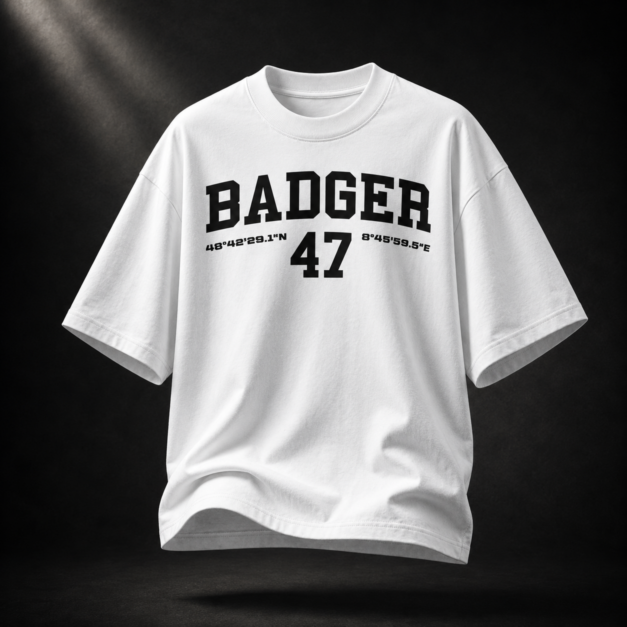Weißes Badger 47 Varsity Oversized T-Shirt mit schwarzem College-Print, schwebend vor dunklem Studiohintergrund
