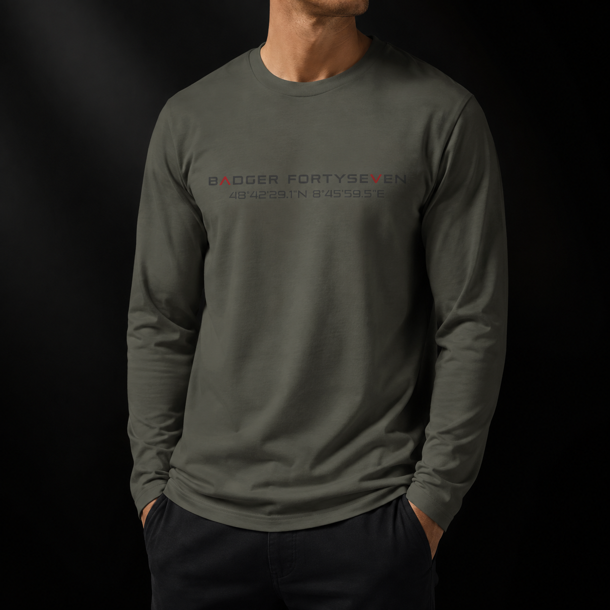 Khakifarbenes Badger FortySeven Organic Longsleeve als Mockup auf schwarzem Hintergrund mit natürlicher Faltenbildung und Brustprint mit Logo und Koordinaten.
