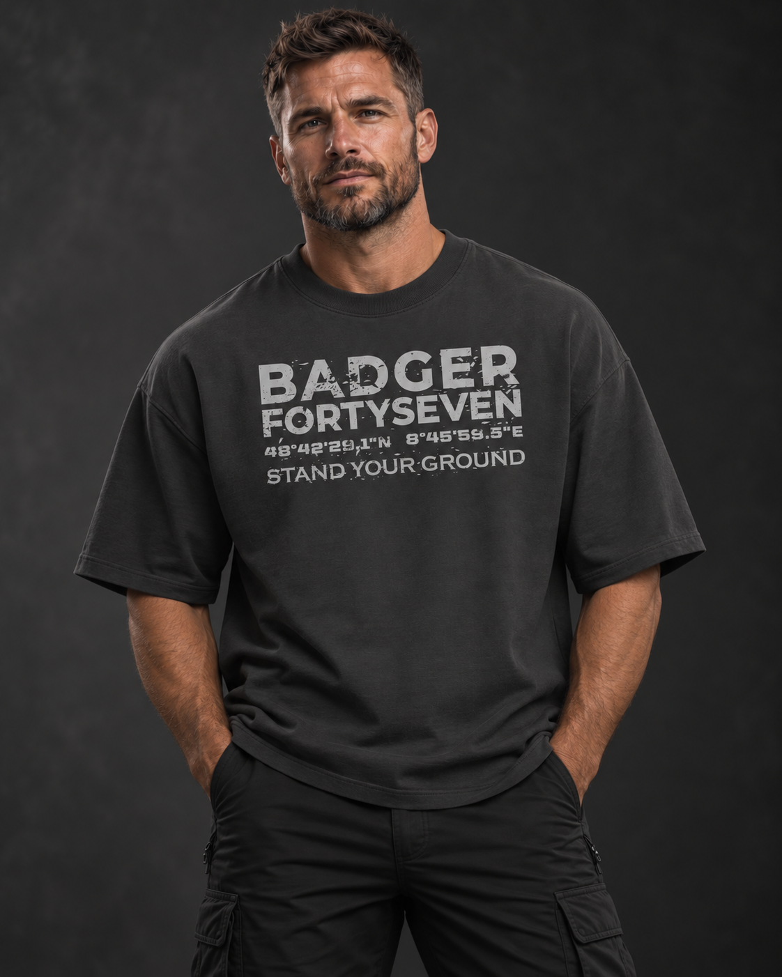 Athletisches Herrenmodel im anthrazitfarbenen BADGER FORTYSEVEN Oversize-T-Shirt mit Statement-Print vor dunklem Studiohintergrund