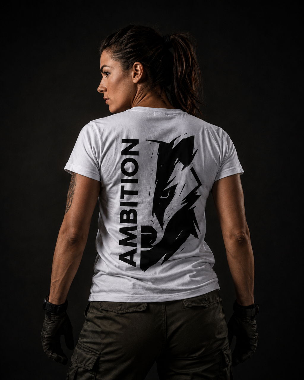 Militärisch inspiriertes Frauenmodel trägt ein weißes badger47 Ambition T-Shirt mit großem schwarzem Rückenprint vor dunklem Hintergrund
