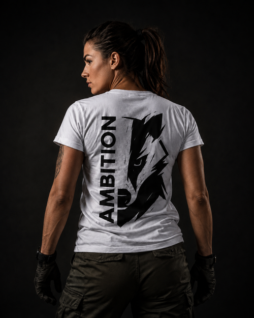 Militärisch inspiriertes Frauenmodel trägt ein weißes badger47 Ambition T-Shirt mit großem schwarzem Rückenprint vor dunklem Hintergrund
