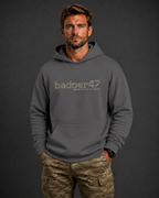 Dunkelblondes Männermodel mit badger47 Boxcut Hoodie in Magnet und Multicam-Hose vor anthrazitfarbenem Studiohintergrund