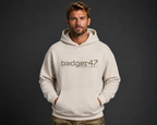 Dunkelblondes Männermodel mit badger47 Boxcut Hoodie in White Sand und Multicam-Hose vor anthrazitfarbenem Studiohintergrund
