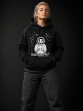 Blondes Frauenmodel Anfang 30 trägt schwarzen Badger47 Hoodie mit Astronauten-Dachs-Print und anthrazitfarbener Utility-Hose vor dunklem Studiohintergrund
