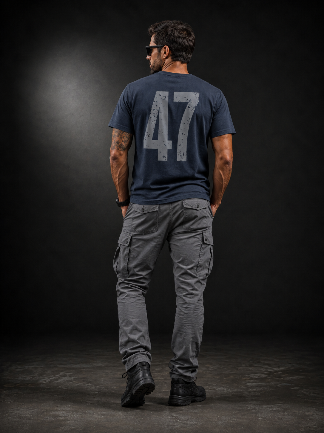 Rückansicht eines männlichen Models im Badger47 Distressed Organic T-Shirt in India Ink Grey mit großem grauem 47-Backprint, kombiniert mit grauer Cargo-Hose und schwarzen Boots vor dunklem Studiohintergrund.