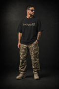BADGER47 FIELD Organic Oversize T-Shirt in Black mit Multicam-Logo, getragen mit Multicam-Cargohose im dunklen Studio
