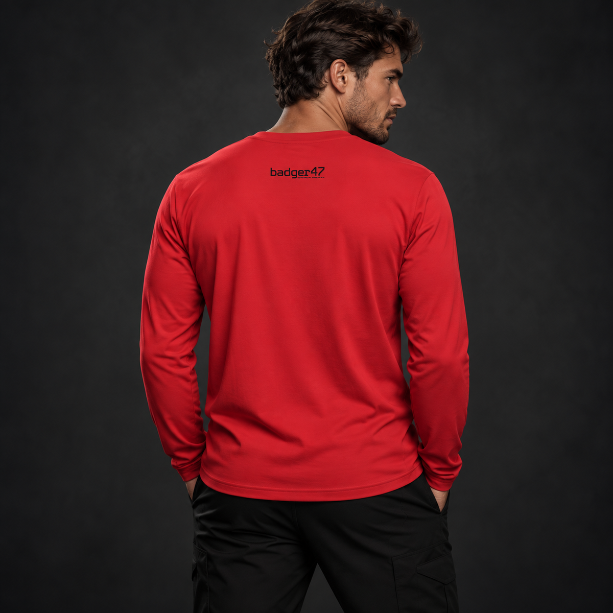 Athletisches männliches Model trägt ein rotes Badger47 Longsleeve mit kleinem schwarzem Badger47 Logo im oberen Rückenbereich vor anthrazitfarbenem Studiohintergrund.