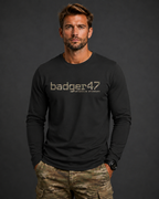 Dunkelblondes Männermodel mit schwarzem badger47 Organic Longsleeve und Multicam-Hose vor anthrazitfarbenem Studiohintergrund