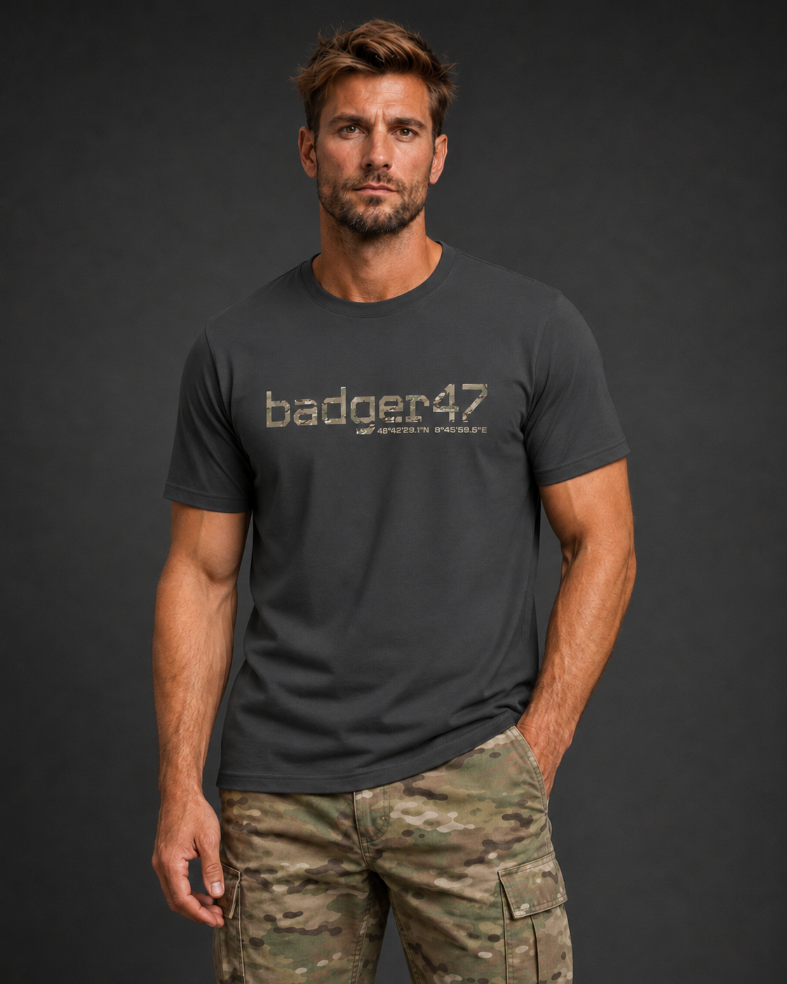 Dunkelblondes Männermodel mit anthrazitfarbenem badger47 Organic T-Shirt und Multicam-Hose vor anthrazitfarbenem Studiohintergrund