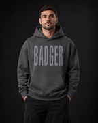 Männermodel trägt einen dunkelgrauen badger47 Oversized Hoodie mit großem BADGER-Print auf der Vorderseite
