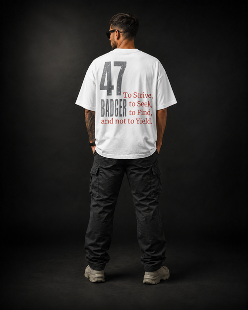 Rückansicht eines männlichen Models im weißen Badger47 Strive Oversized T-Shirt mit großem 47-Badger-Backprint und rotem „To Strive, to Seek, to Find, and not to Yield“-Schriftzug, kombiniert mit schwarzer Cargo-Hose vor dunklem Studiohintergrund.