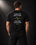 Rückansicht des schwarzen BADGER47 T-Shirts mit „When The Body Stops The Mind Takes Over“-Print und grüner Pulslinie.