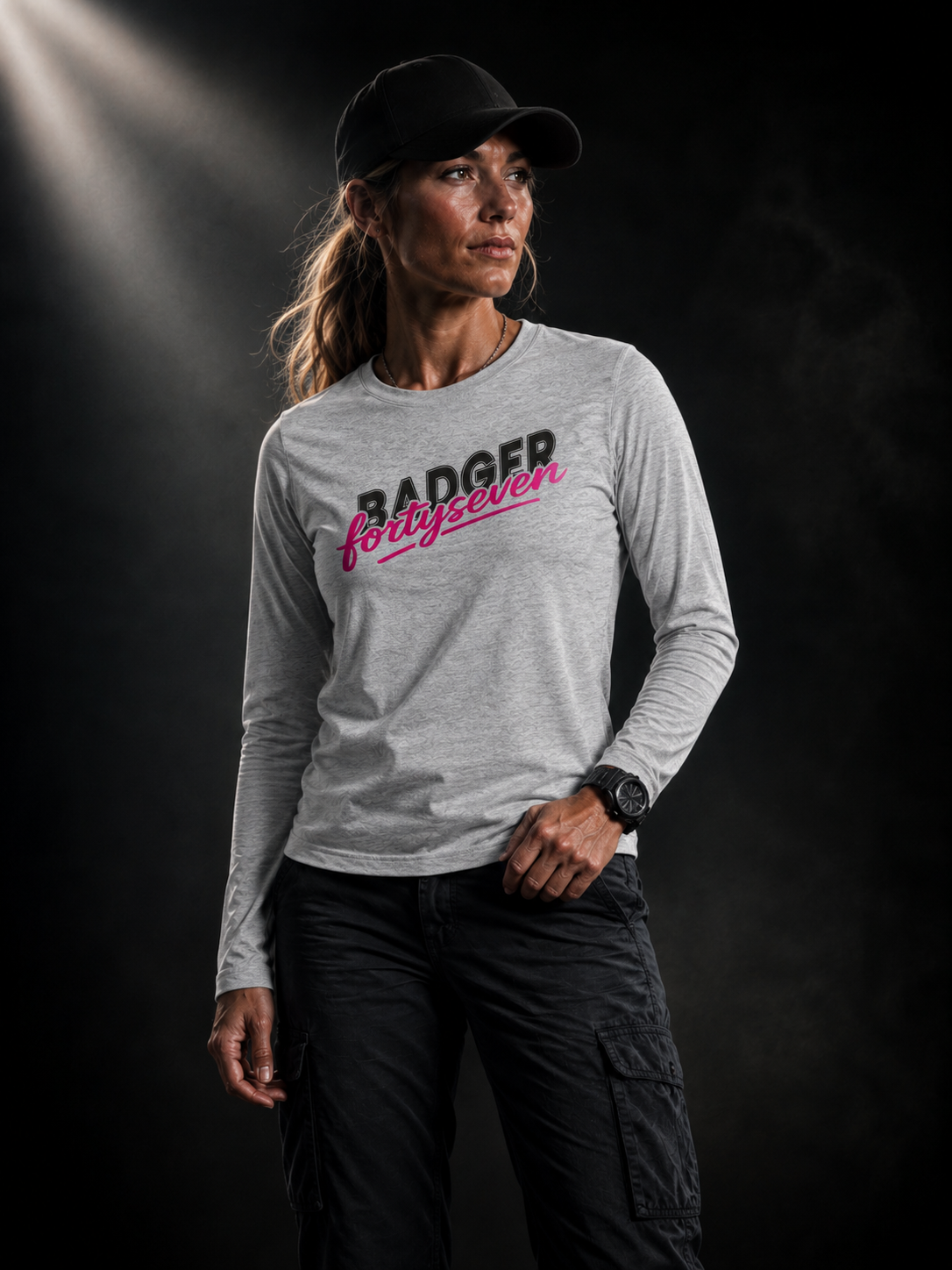 BADGER47 Damen Longsleeve in Heather Grey mit BADGER fortyseven Frontprint, getragen von einem Frauenmodel im dunklen Studio mit markantem Lichteinfall von oben links.